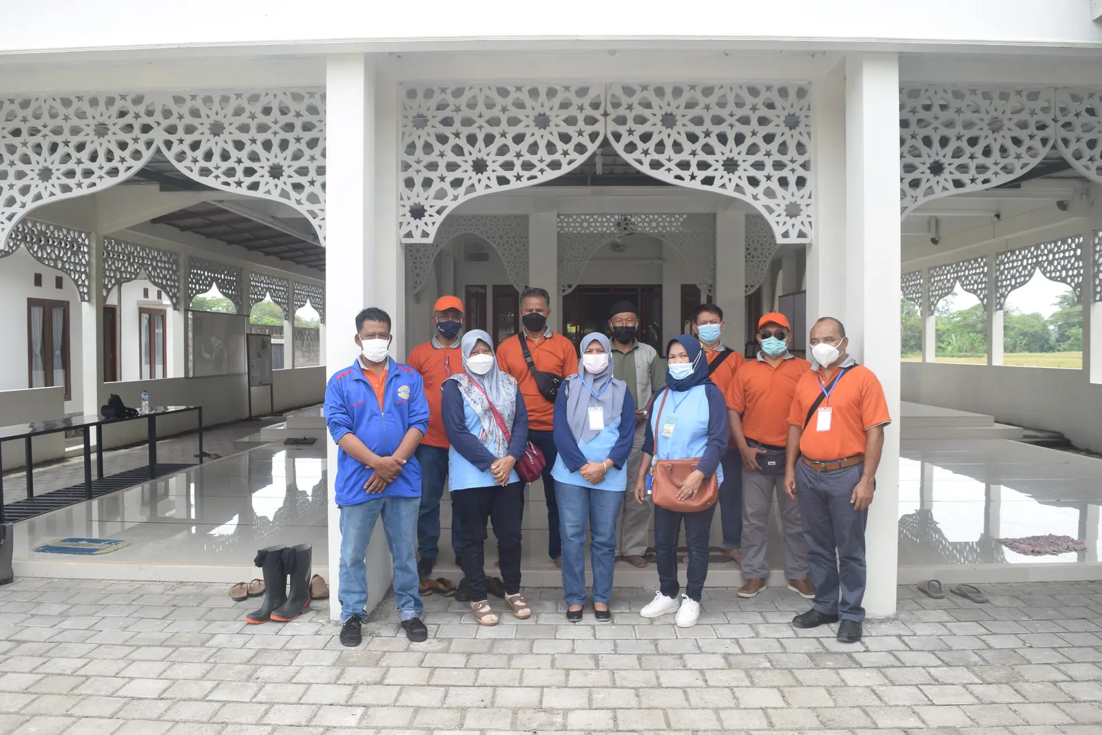 Tim audit K3 berfoto di teras masjid perusahaan mengenakan seragam oranye dan biru dengan masker