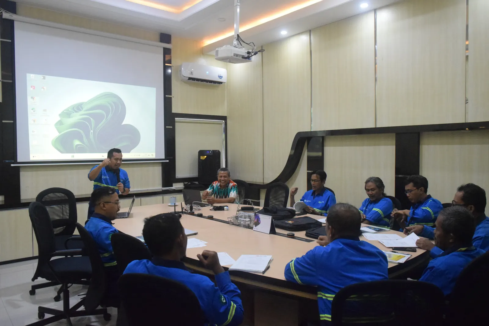 Diskusi kelompok pelatihan K3 di ruang meeting perusahaan dengan peserta berseragam biru