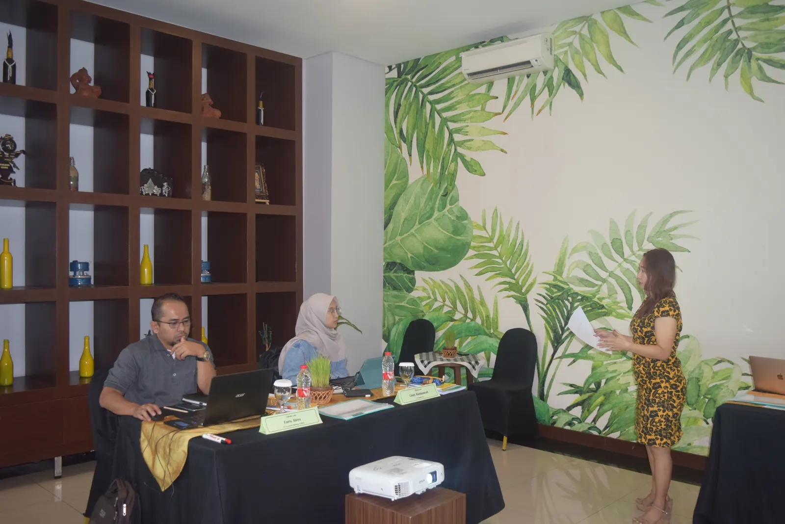 Instruktur menyampaikan presentasi kepada dua peserta di ruang pelatihan hotel dengan dekorasi tropis