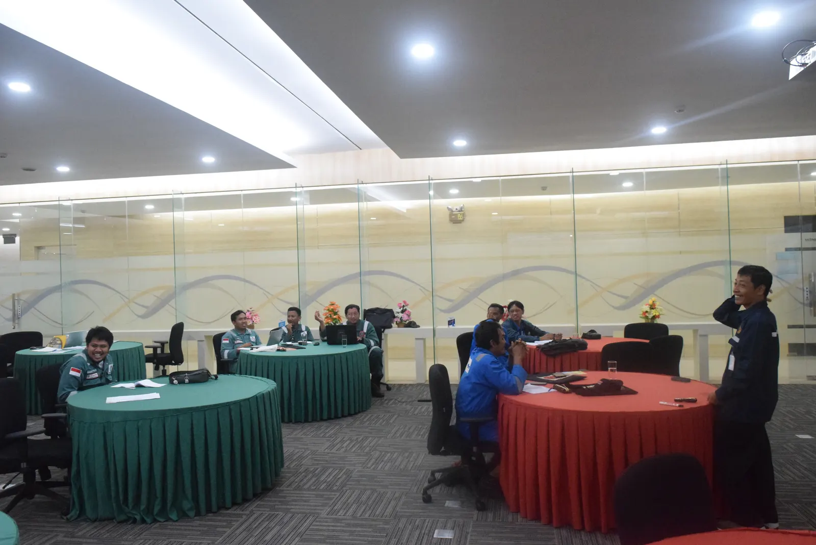 Peserta pelatihan K3 dalam seragam kerja berdiskusi santai di ruang pelatihan modern dengan meja bundar
