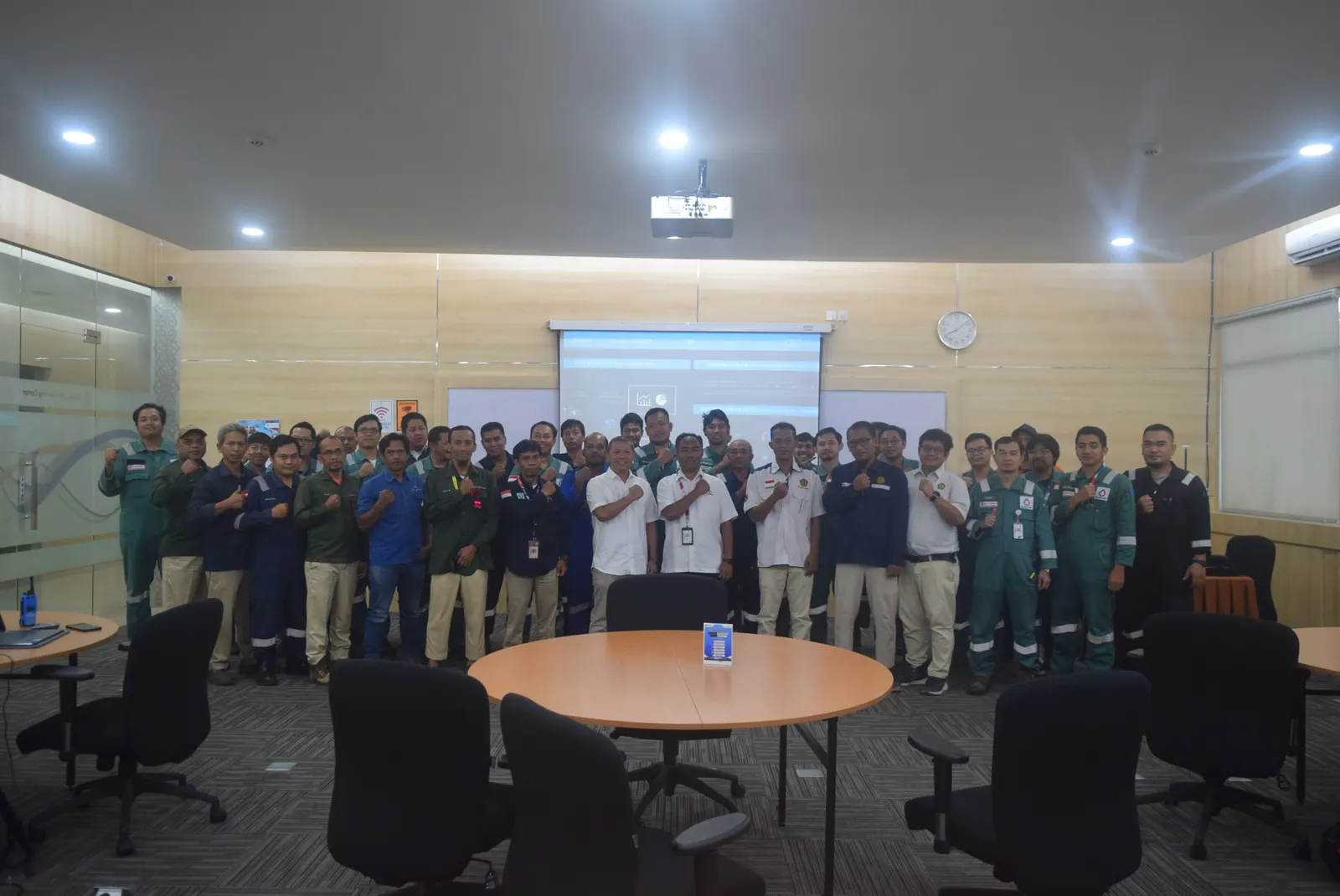 Foto bersama seluruh peserta pelatihan K3 berseragam coverall dan kemeja putih di ruang meeting perusahaan