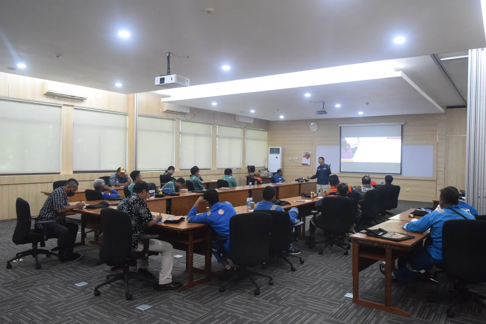 Instruktur menyampaikan materi pelatihan K3 dengan presentasi di ruang kelas modern perusahaan