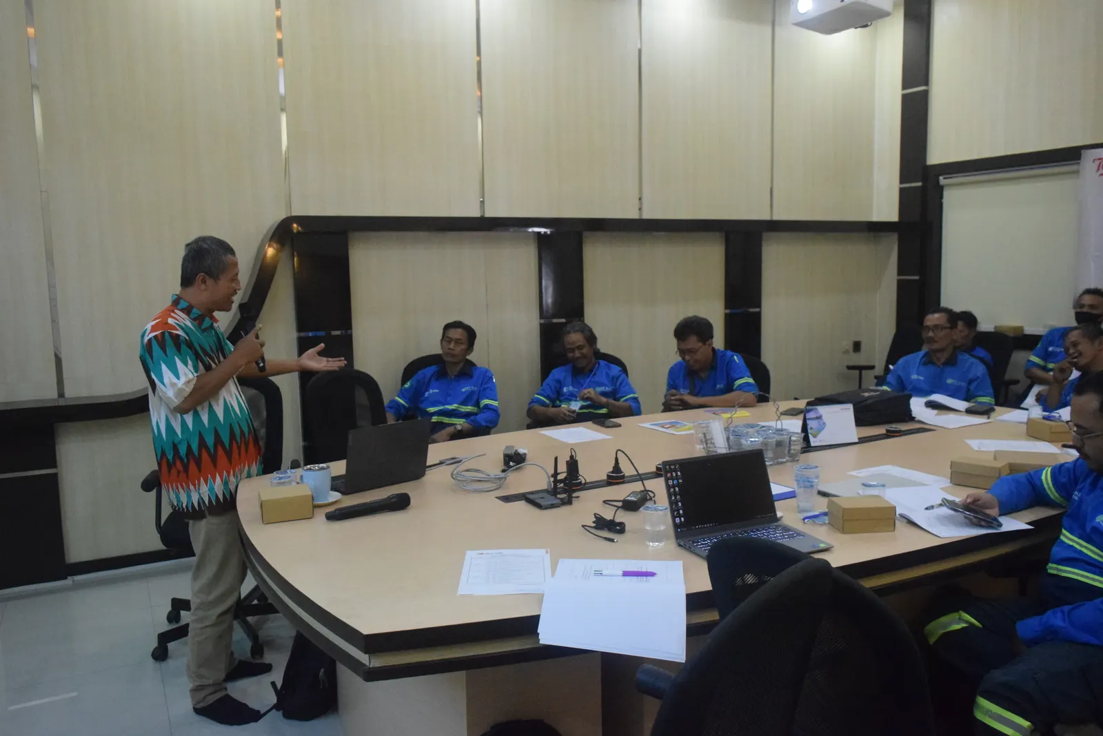 Instruktur senior menyampaikan materi K3 kepada peserta berseragam biru di ruang meeting