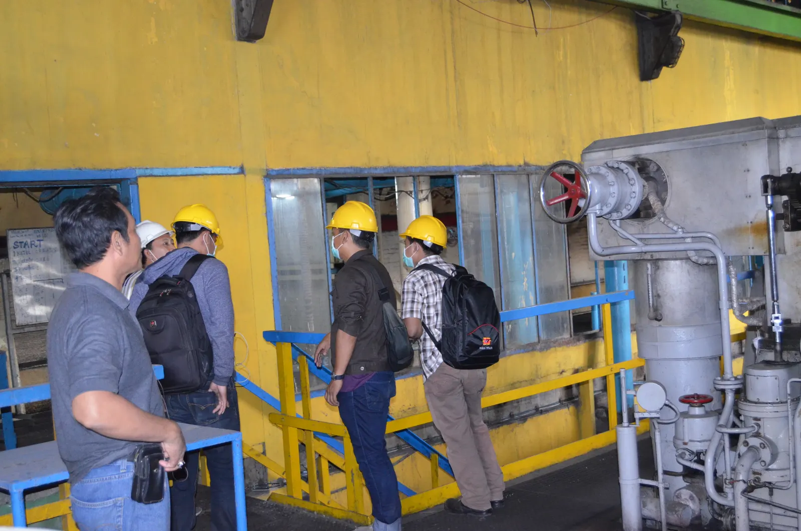 Inspeksi K3 area boiler pabrik oleh tim auditor berhelm kuning mendokumentasikan katup dan instalasi pipa