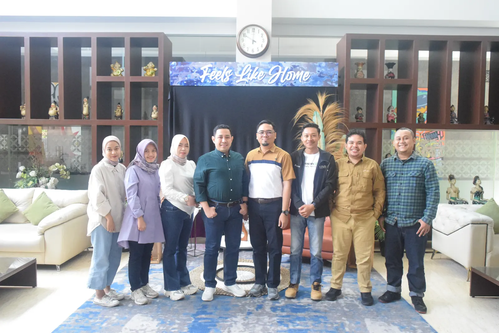 Tim pelatihan berfoto bersama di lobi hotel dengan spanduk Feels Like Home
