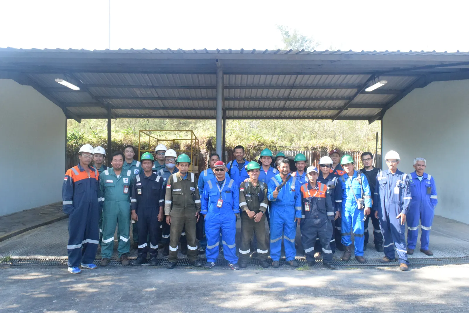 Foto bersama peserta pelatihan K3 berseragam coverall biru dan hijau dengan helm di area fasilitas industri