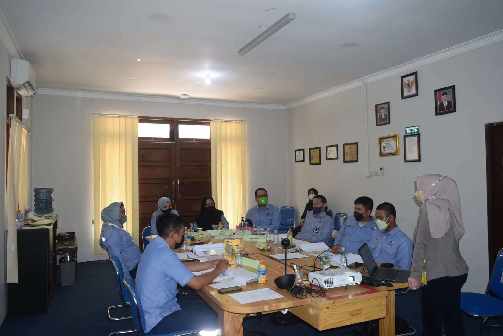 Pelatihan K3 di ruang meeting kantor dengan peserta berseragam biru dan instruktur menyampaikan materi