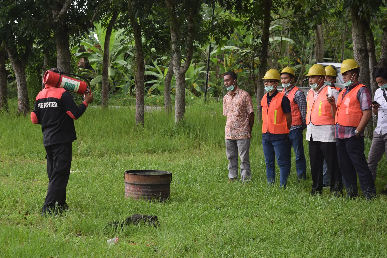 Instruktur fire fighter mendemonstrasikan cara menggunakan APAR kepada peserta berrompi oranye dan berhelm kuning