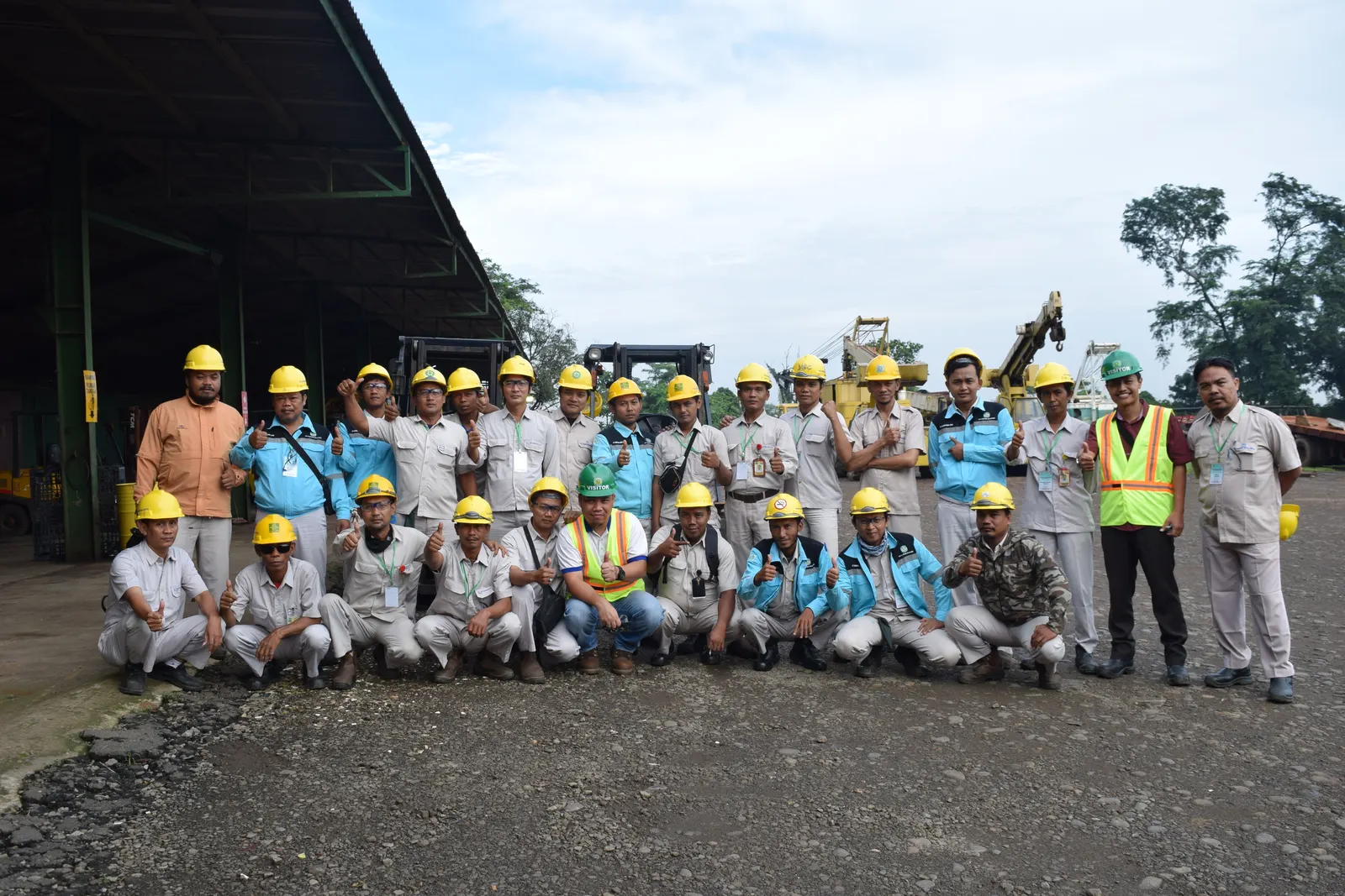 Foto bersama peserta pelatihan K3 operator alat berat berhelm kuning di area logistik dengan forklift dan crane