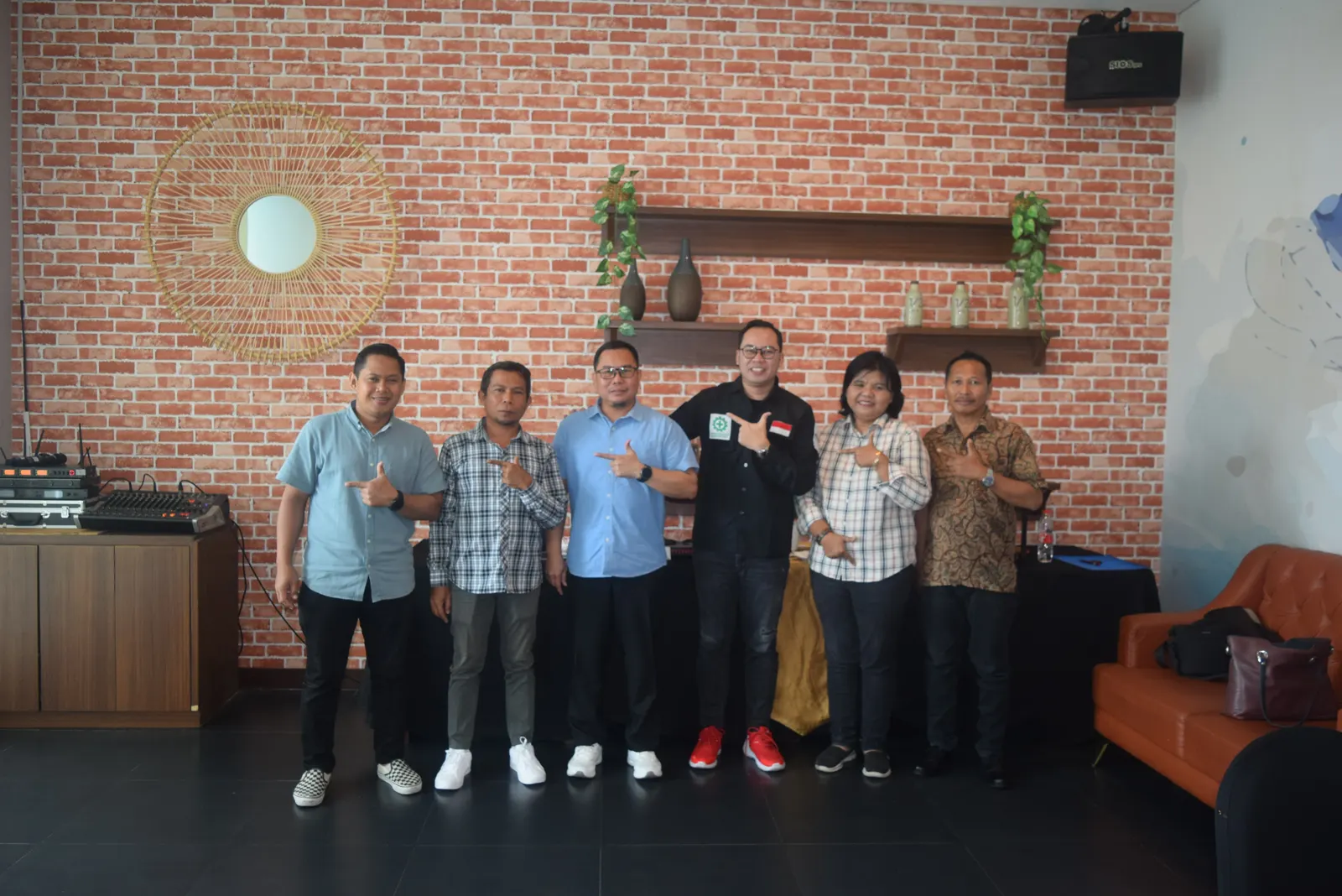 Tim instruktur dan klien berfoto bersama di ruangan dengan dinding bata merah ekspos