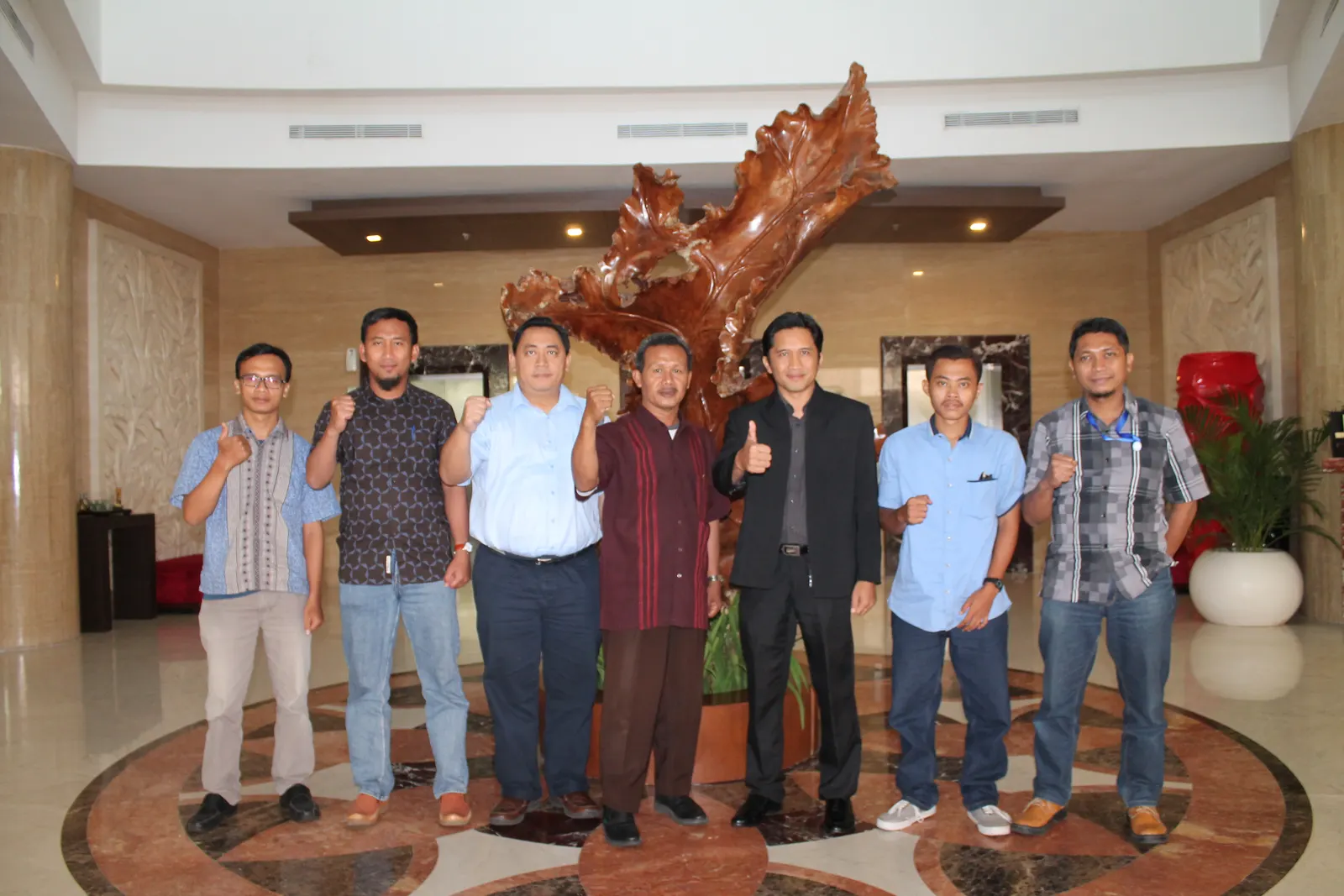 Tim instruktur dan peserta berfoto bersama di lobi hotel mewah dengan patung kayu besar