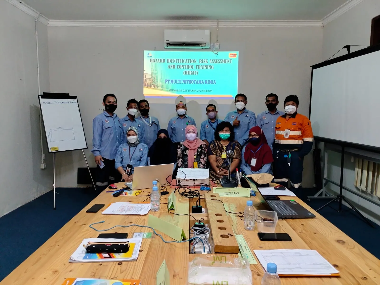 Peserta pelatihan HIRAC PT Multi Nitrotama Kimia berfoto bersama dengan slide presentasi di ruang meeting pabrik