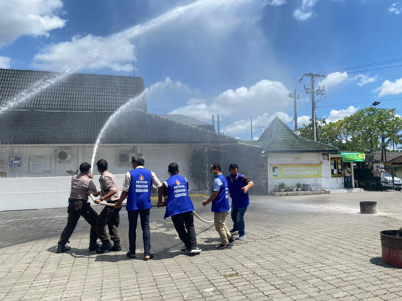 Tim petugas pemadam kebakaran berseragam biru mempraktikkan penggunaan selang pemadam air di halaman gedung