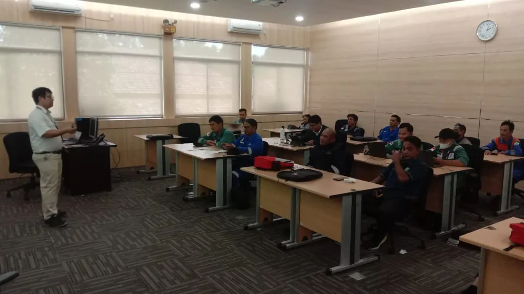 Instruktur menyampaikan materi pelatihan K3 di ruang kelas perusahaan kepada peserta berseragam coverall
